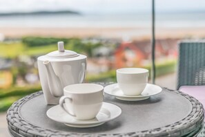 Ein Tisch mit einem weißen Teekännchen und zwei Tassen auf einer gewebten Untertasse, mit Blick auf eine schöne Aussicht.