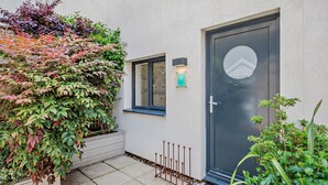 A building entrance with a dark door, a small window with blinds, and a green sign above the door. - Whitehaven - Luxury Cottages (Woolacombe)