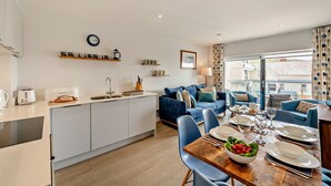 A modern kitchen with a dining area, a sofa, and a view of the outside. - Whitehaven - Luxury Cottages (Woolacombe)