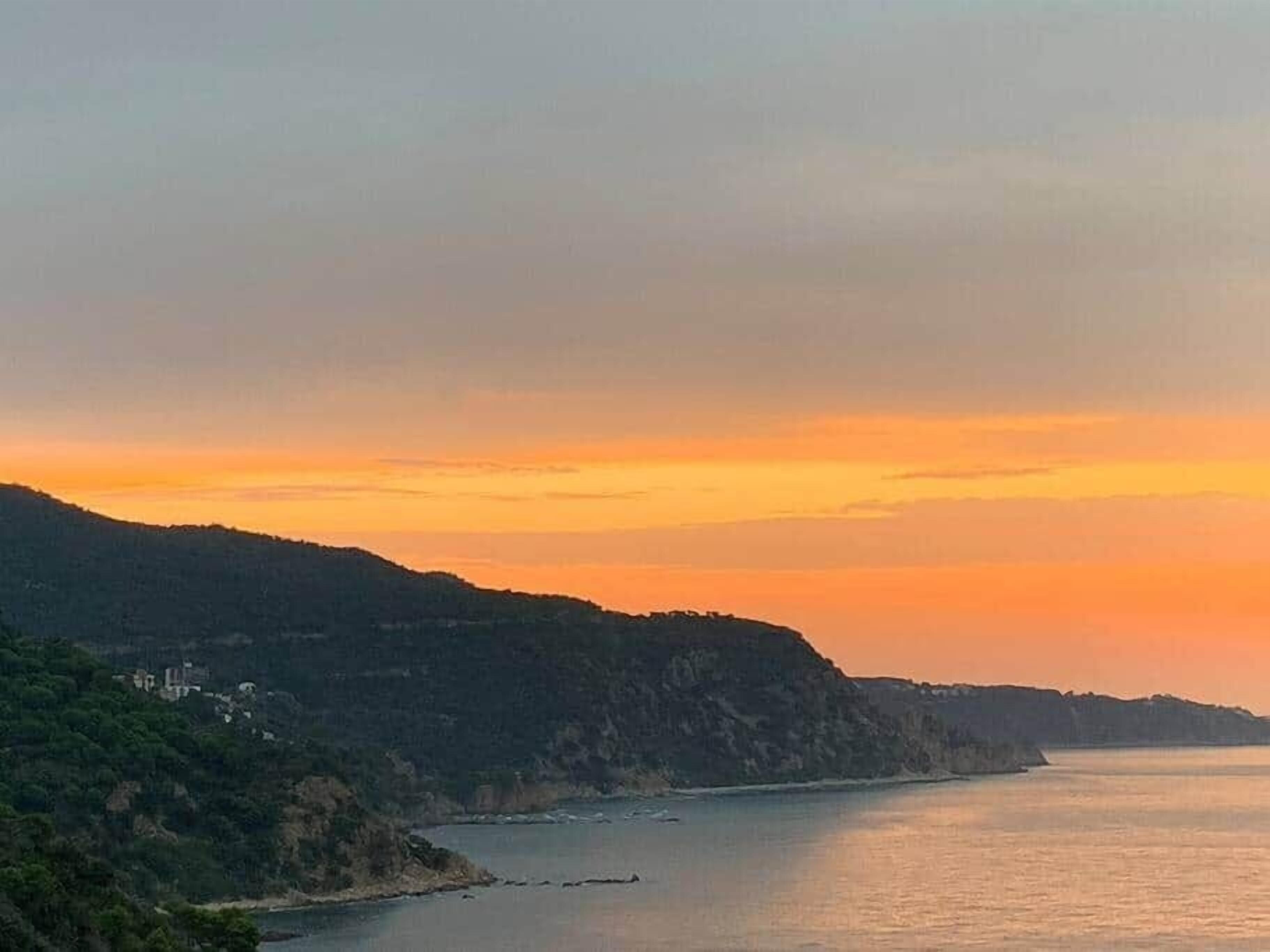 A coastal landscape with a river, hills, and a sunset.