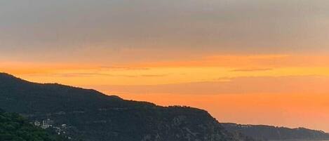 A coastal landscape with a river, hills, and a sunset.