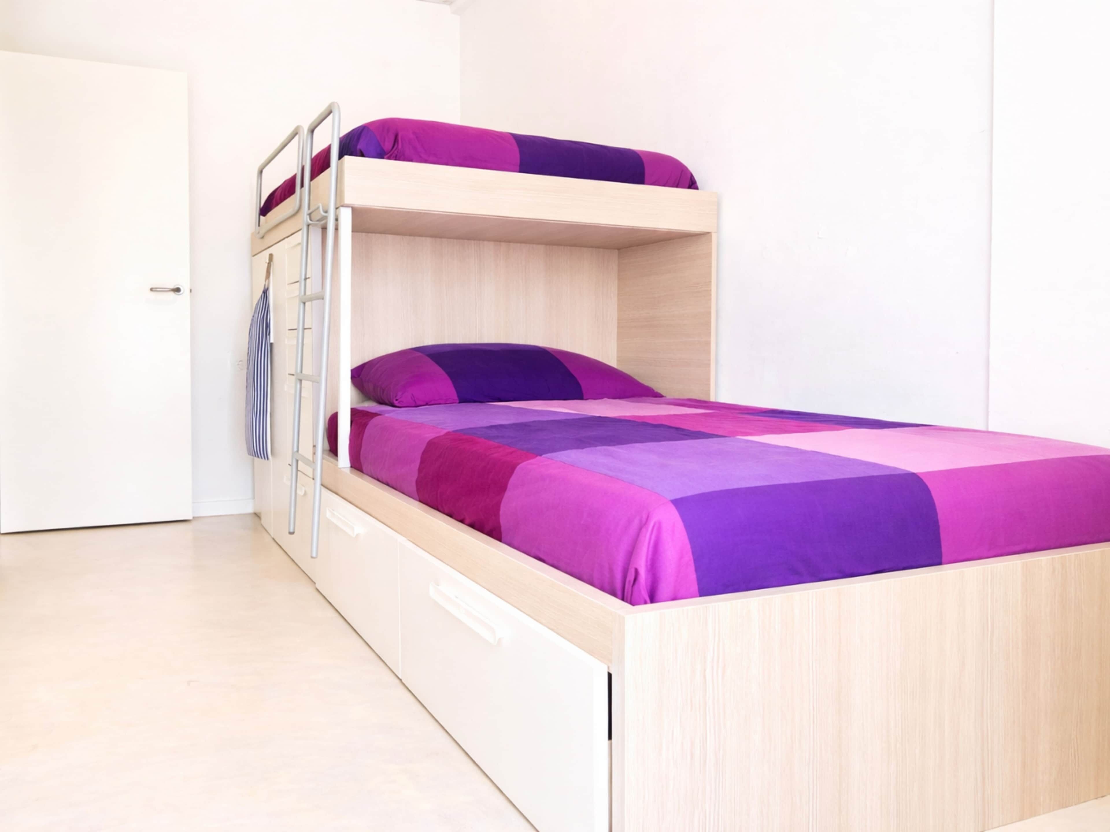 Un lit superposé avec une structure en bois et une couvre-lit aux couleurs violette et rose.