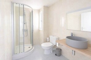 Ein modernes Badezimmer mit einer gläsernen Duschkabine, einer Toilette, einem Waschbecken mit großem Spiegel und einem Mülleimer.