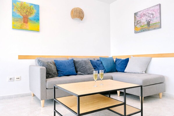 Un salon moderne avec un canapé gris, des coussins bleus, une table basse en bois et deux coupes à champagne.