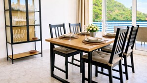 Comedor con mesa de madera, sillas negras, vitrina con copas de vino y vistas a zonas verdes a través de amplios ventanales.