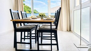 Una mesa de comedor con sillas, un florero y una lámpara en una habitación con ventanas amplias.