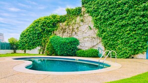 Una piscina con borde curvo, rodeada de una zona pavimentada y abundante césped verde.