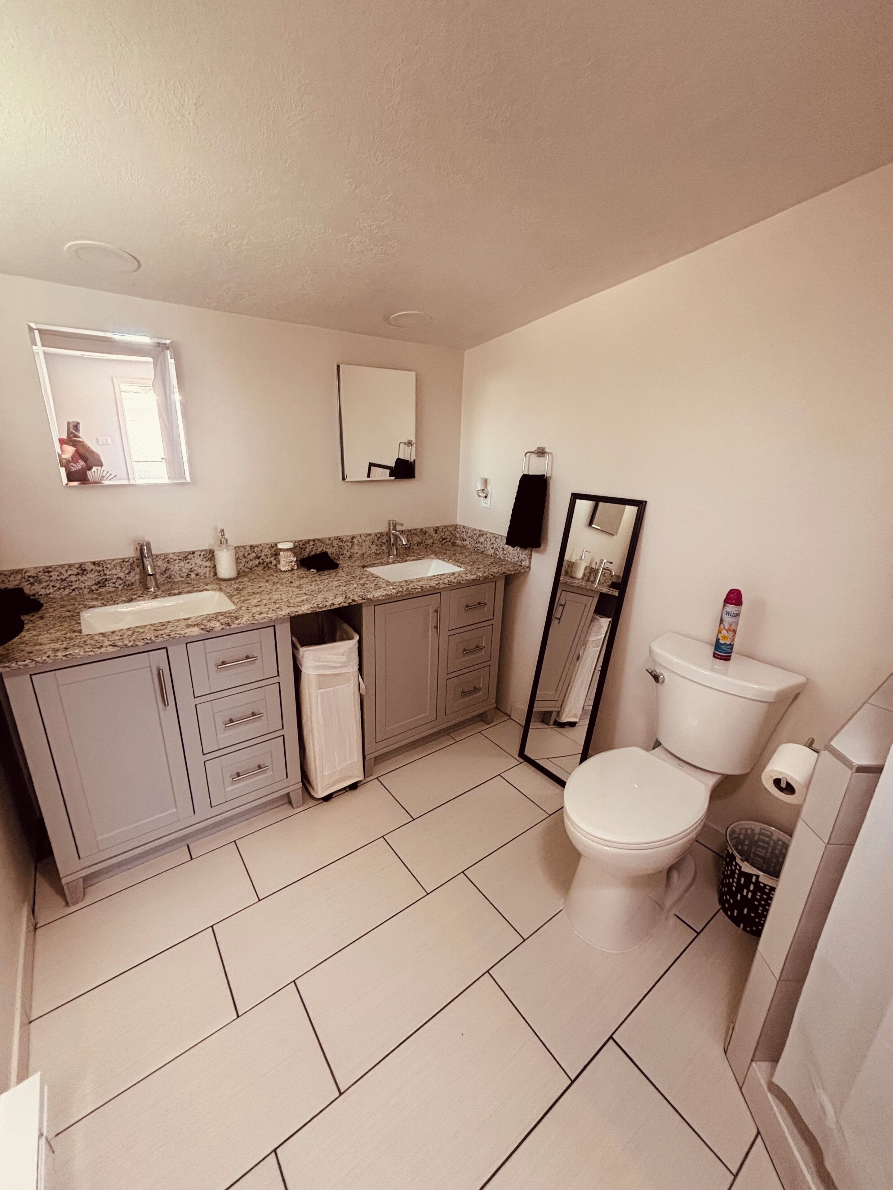 A bathroom with a sink, mirror, toilet, and trash bin.
