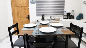 A dining area with a wooden table set for four, black chairs, a clock, and kitchen appliances. - CABO DOWNTOWN STUDIOS: 2BR Queen apt fully equipped Downtown steps to marina (Cabo San Lucas)