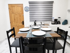 A dining area with a wooden table set for four, black chairs, a clock, and kitchen appliances. - CABO DOWNTOWN STUDIOS: 2BR Queen apt fully equipped Downtown steps to marina (Cabo San Lucas)