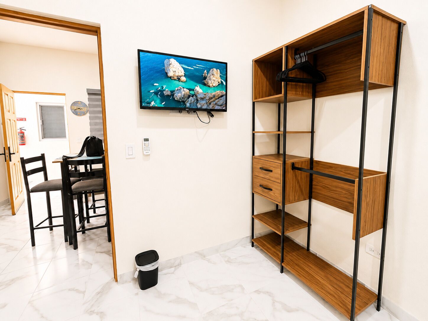 A room with a wooden desk, chairs, a television mounted on the wall, and a built-in wooden shelving unit.