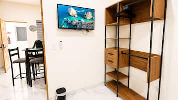 A room with a wooden desk, chairs, a television mounted on the wall, and a built-in wooden shelving unit.
