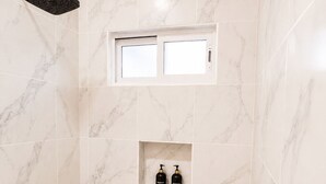 A bathroom with marble tiles, a showerhead, a window, and two bottles on a shelf. - CABO DOWNTOWN STUDIOS: 2BR Queen apt fully equipped Downtown steps to marina (Cabo San Lucas)