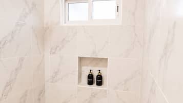 A bathroom with marble tiles, a showerhead, a window, and two bottles on a shelf.