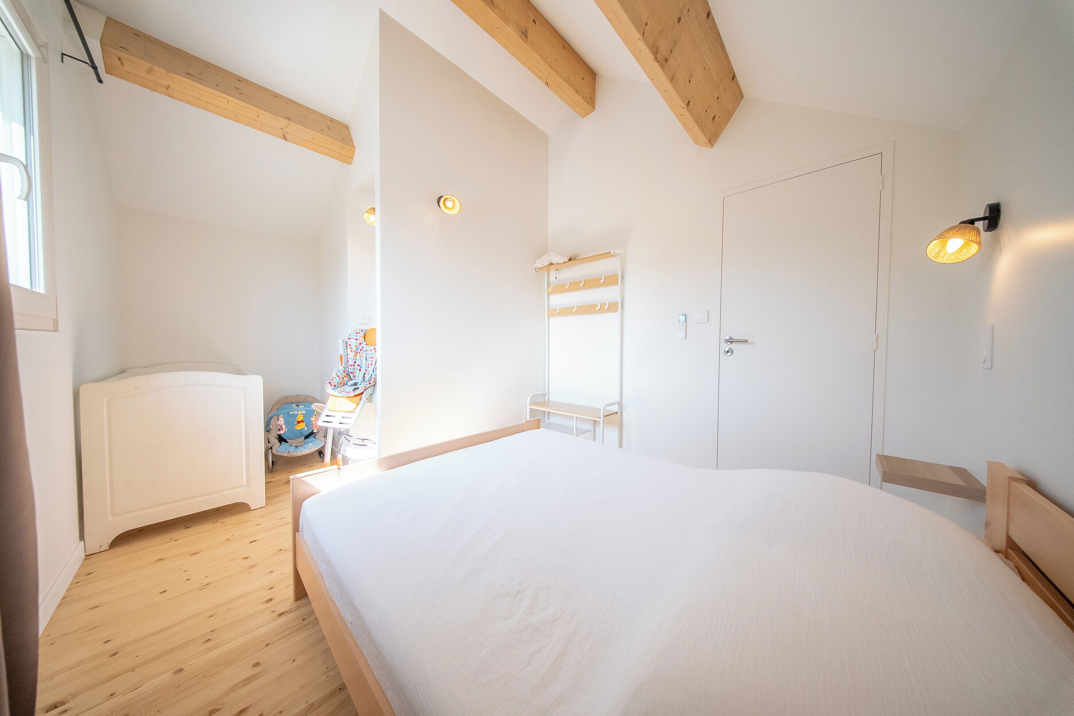Ein Schlafzimmer mit einem großen Bett, Holzbalken, einer weißen Tür und einer kleinen Sitzecke mit Stuhl und Tisch.
