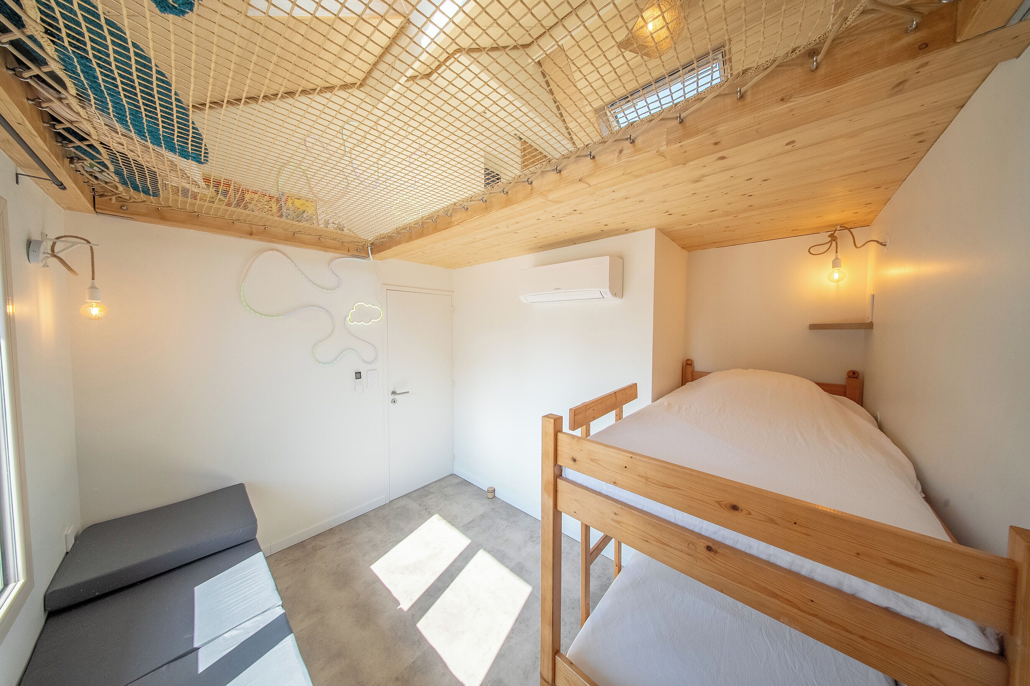 A room with a bunk bed, a small seating area, a wall-mounted air conditioning unit, and a window with a view.