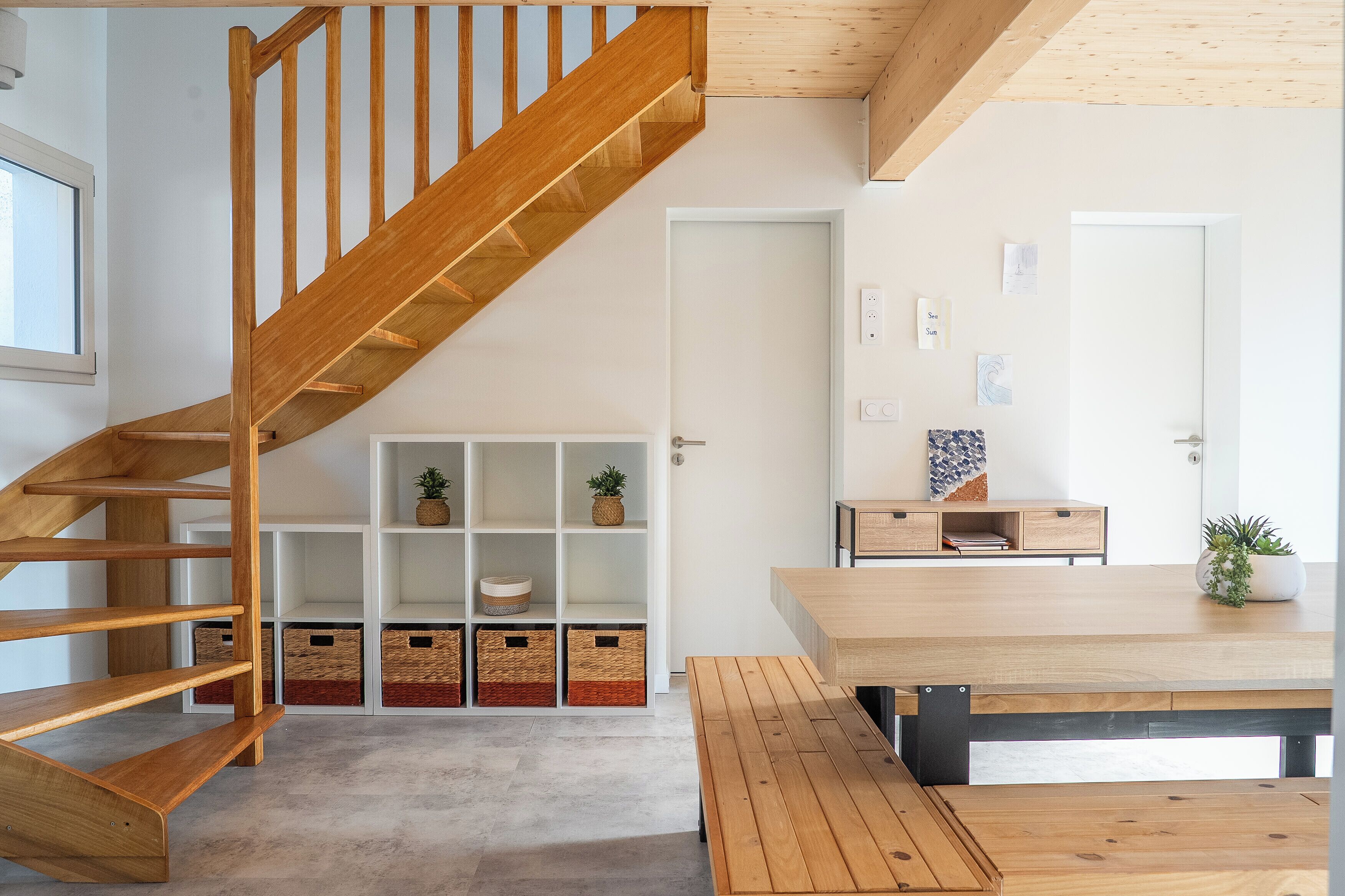 Een modern interieur met een houten trap, een witte muur met kunstwerk en een houten eettafel.
