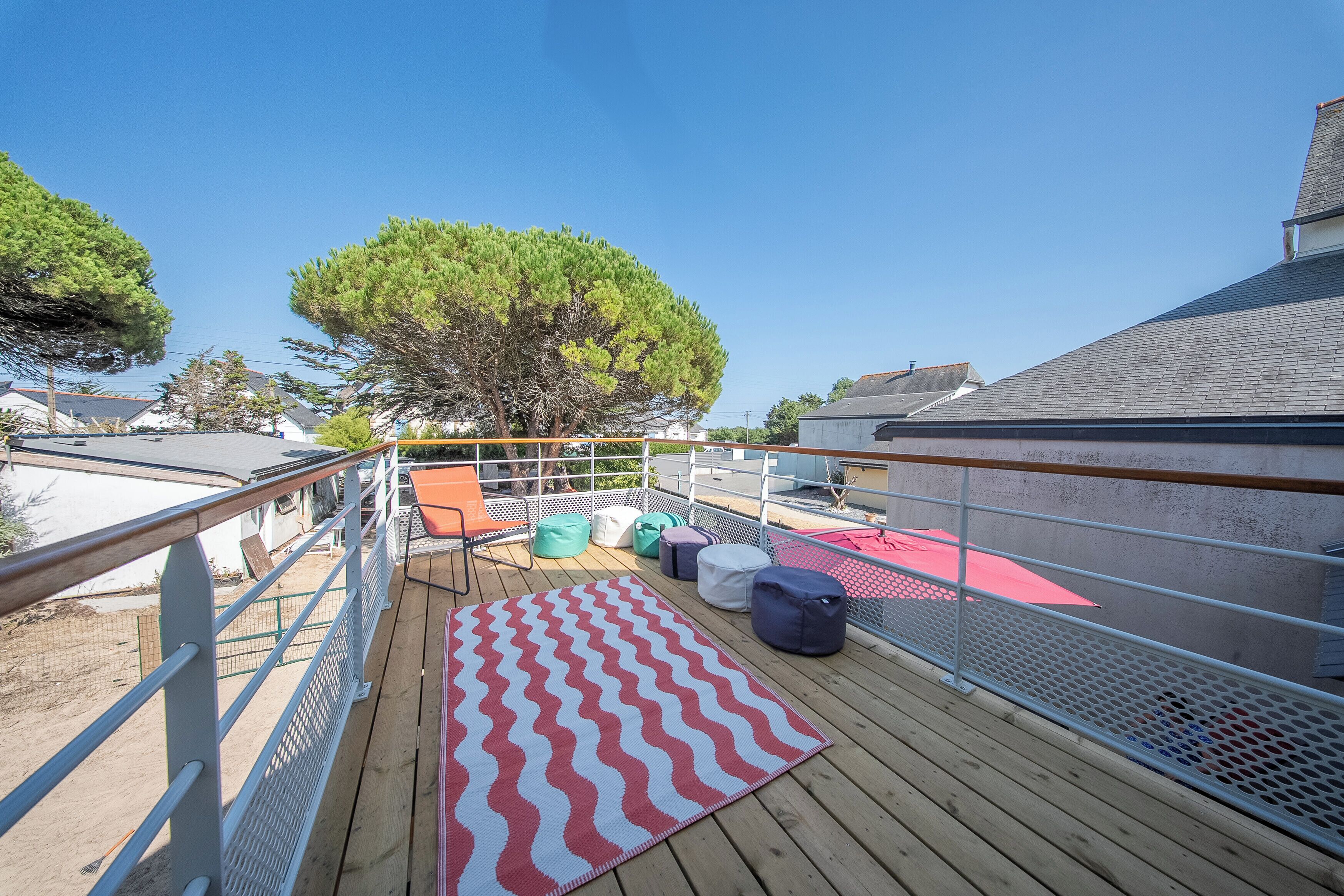 A wooden deck with a red and white patterned rug, outdoor seating, and a metal railing.