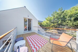 Eine Holzterrasse mit einer rot-weißen Zickzack-Isomatte, einem Metallgeländer und einem einzelnen orangefarbenen Stuhl.