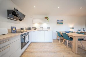 Eine moderne Küche mit eingebautem Ofen, Mikrowelle und Spüle. Ein Essbereich mit Holztisch und Stühlen ist ebenfalls vorhanden.