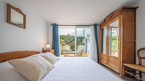 Ein Schlafzimmer mit einem Bett, einem Holzschrank, einem Sessel und einer Glastür zu einem Balkon.