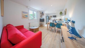 Ein modernes Wohnzimmer mit einem roten Sofa, einem Essbereich mit Holztisch und -stühlen, einer Küche im Hintergrund und Blick auf Grünflächen außerhalb.