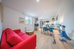 Ein modernes Wohnzimmer mit einem roten Sofa, einem Essbereich mit Holztisch und -stühlen, einer Küche im Hintergrund und Blick auf Grünflächen außerhalb.