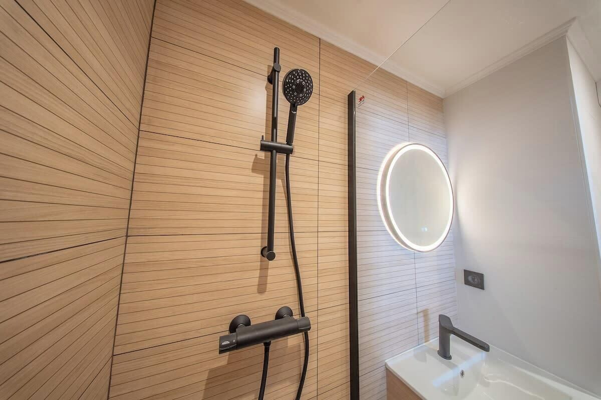 A modern bathroom with a wooden panel wall, a handheld showerhead, a wall-mounted mirror, and a white sink.