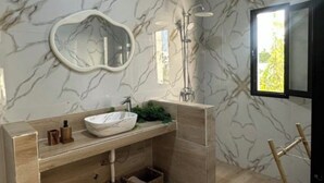 A modern bathroom with a marble backsplash, a round mirror, a sink, and a shower area.