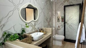 A modern bathroom with a marble wall, a round mirror, a wooden vanity, a toilet, and a shower area.