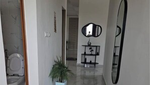 A hallway with a marble floor, a potted plant, a rug, a mirror, and a door leading to a bathroom.
