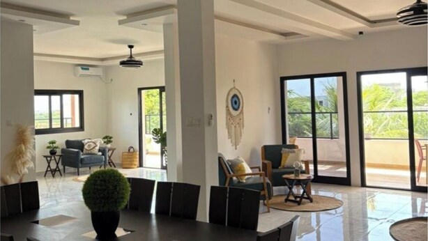 Un comedor amplio con una mesa grande y sillas, un ventilador de techo y vistas a un espacio exterior a través de puertas correderas.