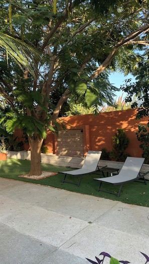 A patio area with a tree, a wall, and two lounge chairs.
