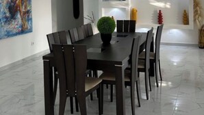 Un comedor moderno con suelo de mármol, una mesa central con sillas, una lámpara en el techo y una pared con estanterías.