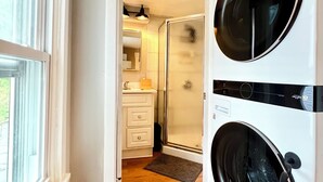A laundry room with two front-loading washing machines, a glass shower door, a white sink, and a wooden floor.