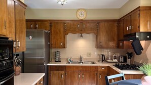 Een keuken met houten kasten, een roestvrijstalen koelkast, een spoelbak en een eethoek met een tafel en stoelen.