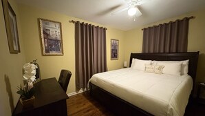 Een hotelkamer met een bed, een bureau, een stoel, een plafondventilator en twee afbeeldingen in lijsten aan de muur.