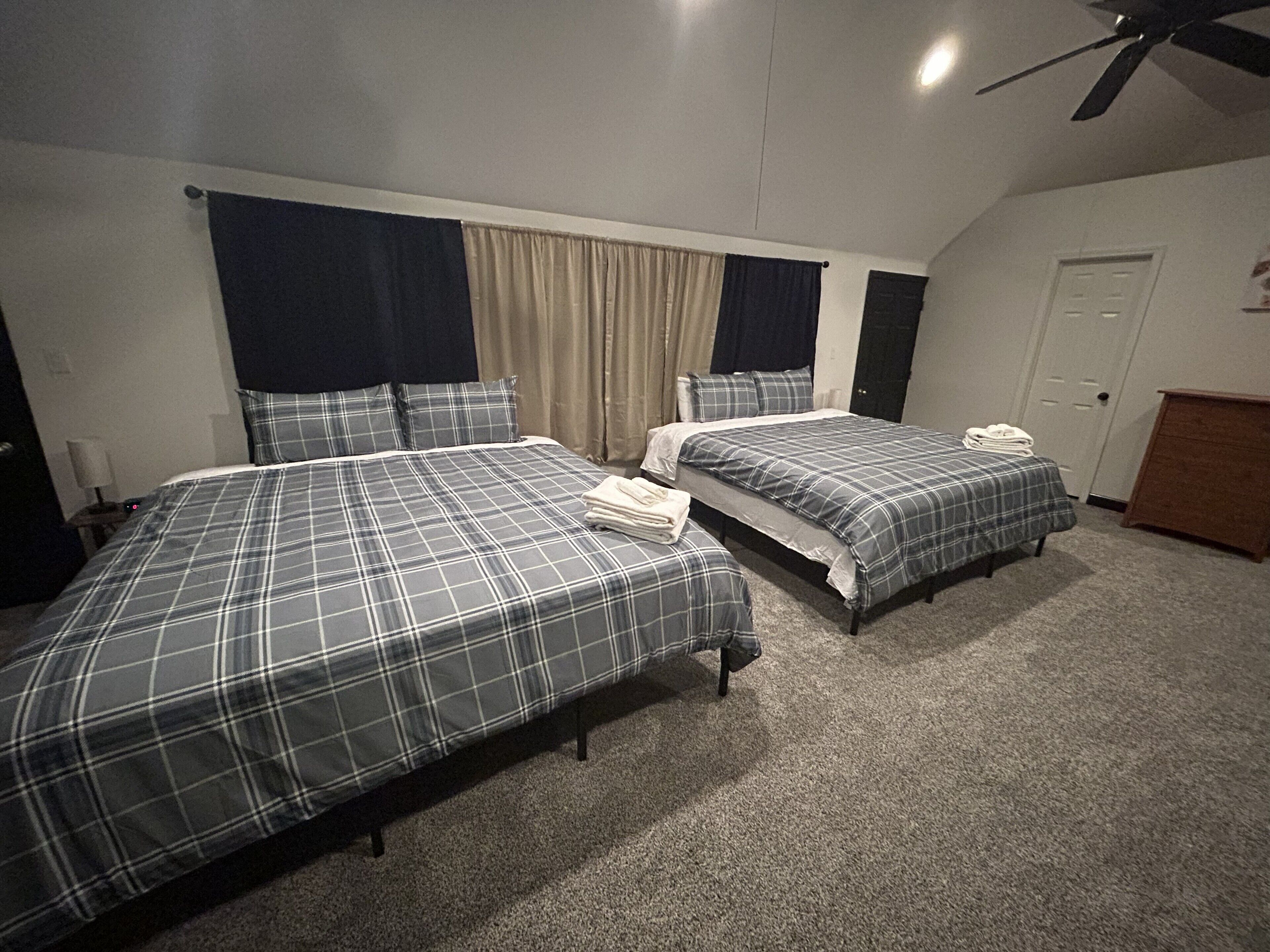 A room with two beds, a ceiling fan, a door, and a small wooden cabinet.