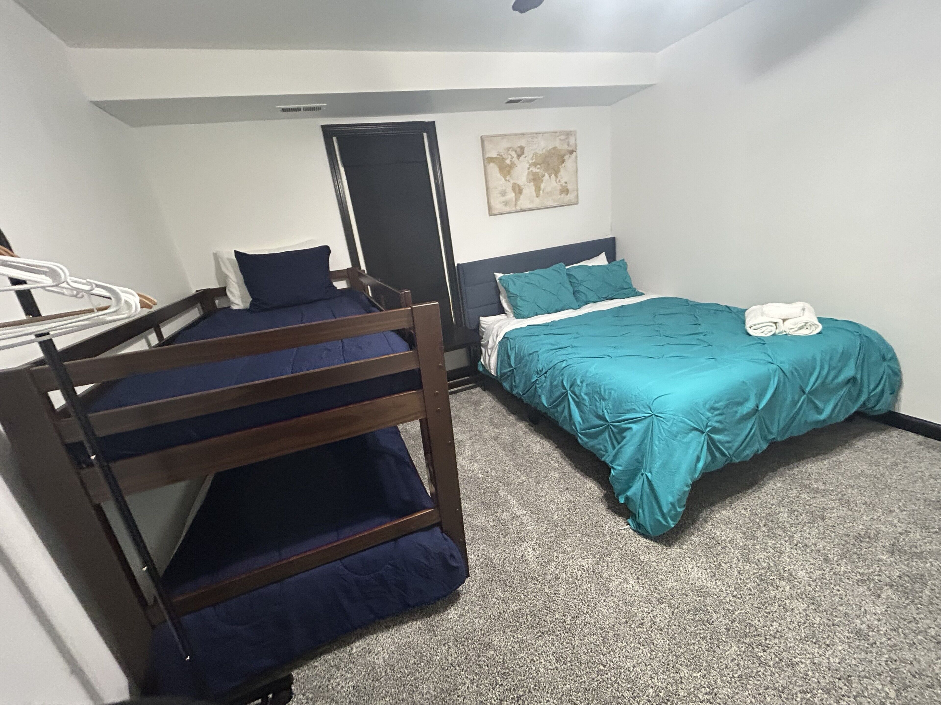 A room with bunk beds, a single bed, a world map on the wall, and a door.