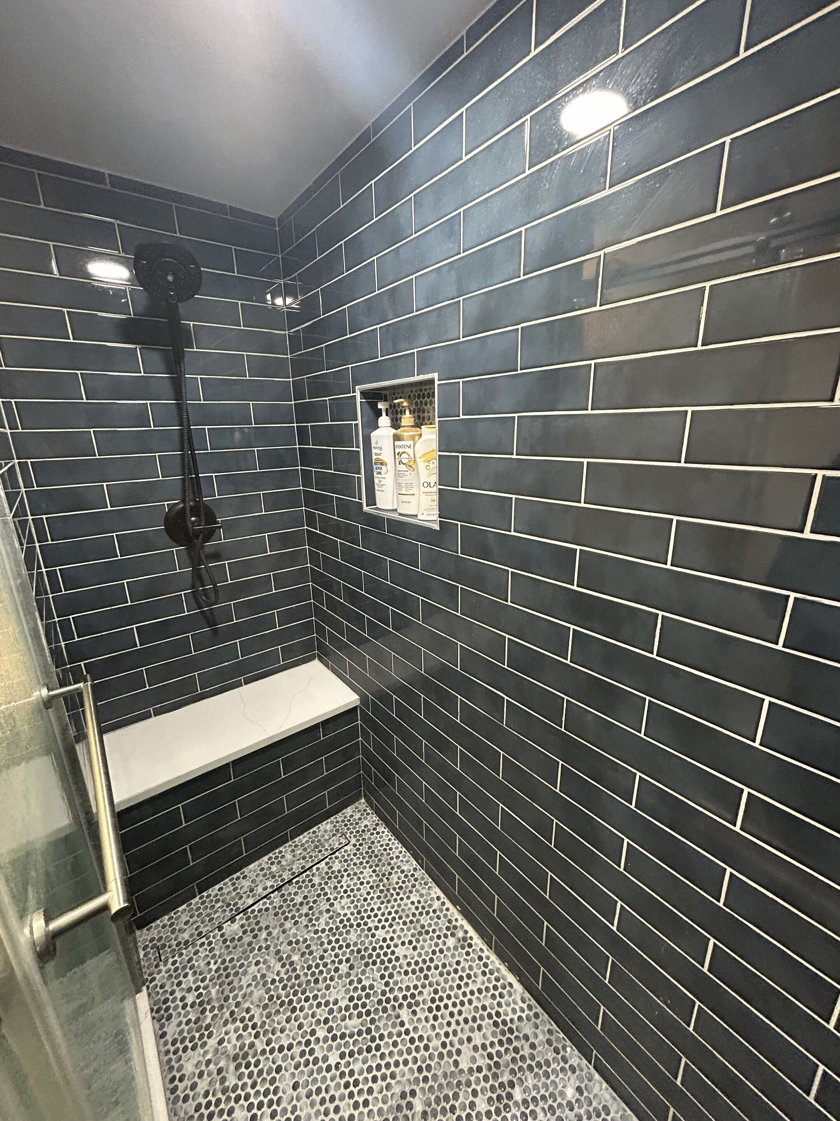 Une douche aux carreaux noirs, un banc et une étagère avec des articles de toilette.