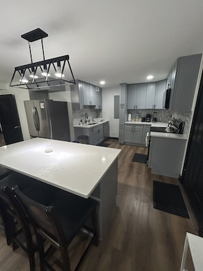 A modern kitchen with a marble countertop, stainless steel appliances, and light wood flooring.