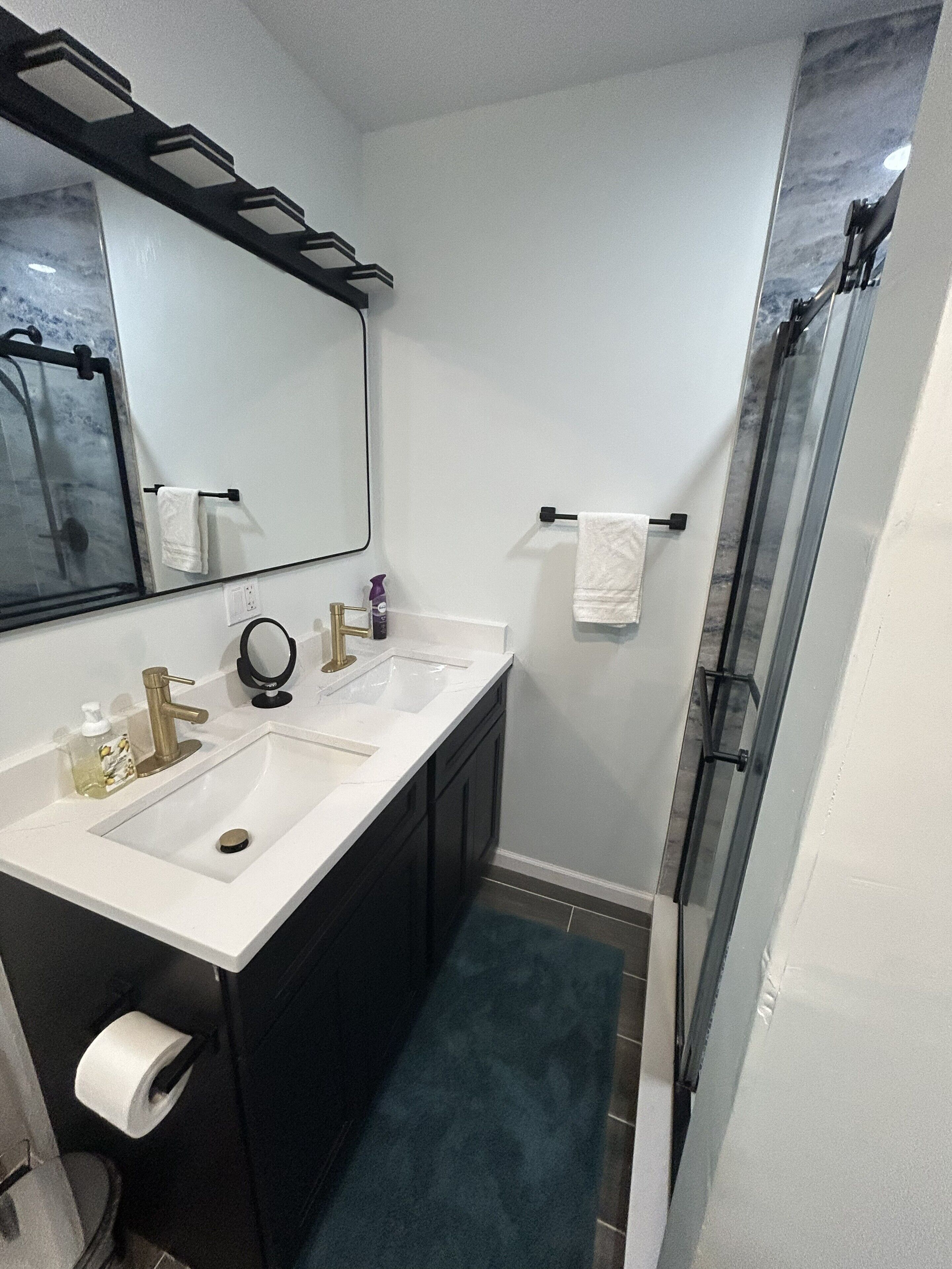 A bathroom with a white sink, two mirrors, a glass shower enclosure, and a dark-colored vanity.