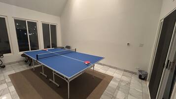 A ping pong table in a room with a tiled floor, large windows, and a door.