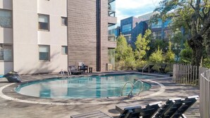 Une piscine avec des chaises longues, une terrasse en bois et un bâtiment à l’architecture moderne.