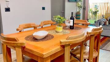 A wooden dining table with six chairs, a white bowl, a bottle of wine, and a vase with green plants.