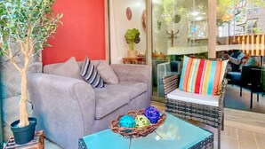 Un salon avec un canapé gris, un fauteuil en osier, une table basse en verre et une plante en pot.