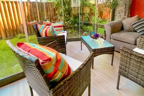 Un patio con mobiliario de mimbre, una mesa y vistas a un jardín.