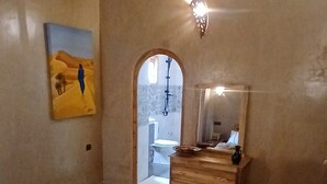 A room with a sofa, a small round table, a wooden dresser, a mirror, and a painting on the wall. - La Colline Verte Dar Ait El Abass  (Skoura)