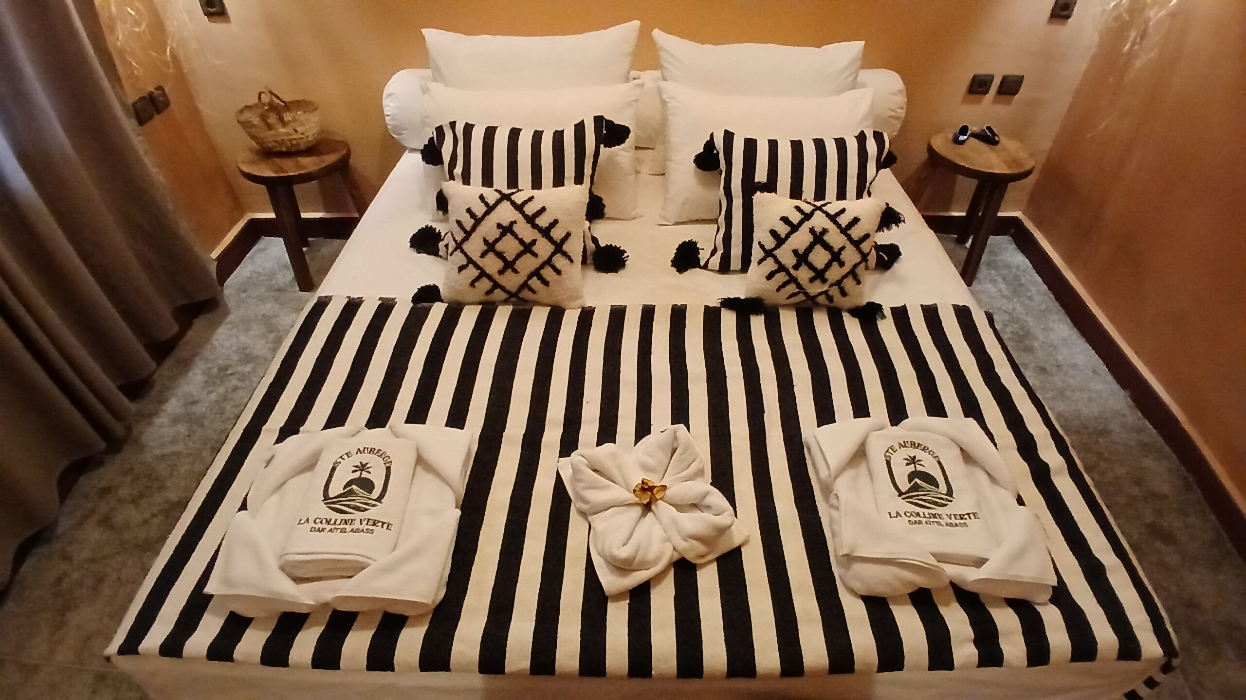 A hotel room with a striped bedspread, pillows with a black and white pattern, and two towels with a logo.