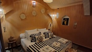 A hotel room with a bed, pillows, a small table, and wall decor.